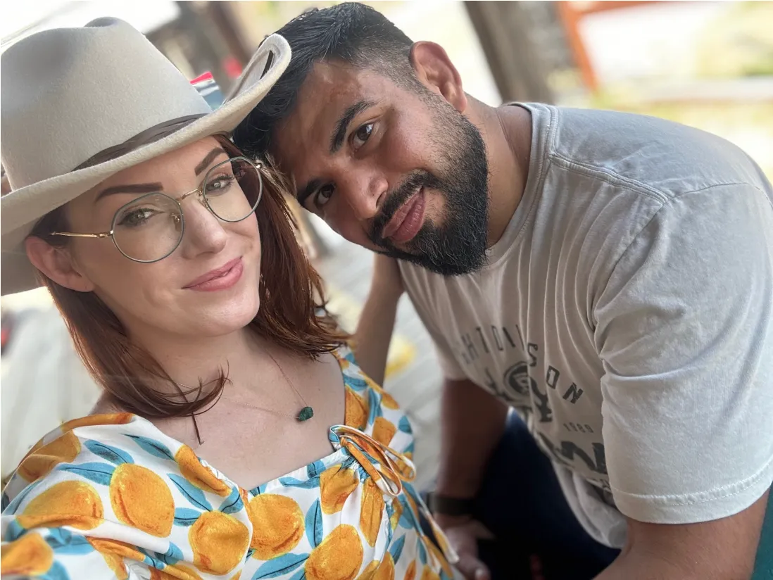 A couple leaning their heads together and smiling, she in a cowboy hat and glasses